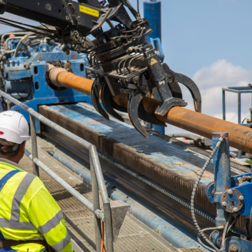 Man in yellow PPE operating a gripper for a drill rig